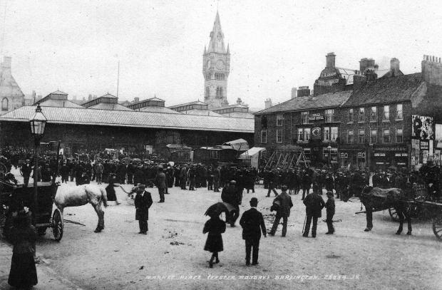 Darlington and Stockton Times: Darlington Market Place on Easter Monday. Outside the Bulls Head Hotel on Bakehouse Hill are shuggyboat swings, and makeshift tents so it looks as if a circus or menagerie has arrived to entertain the Bank Holiday crowds. There's an empty window on